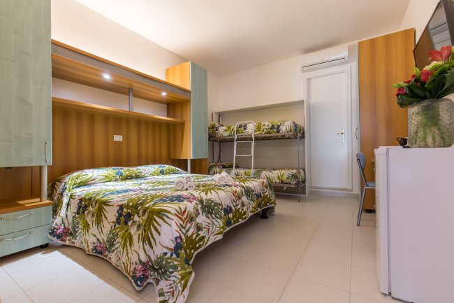 Camera con letto matrimoniale, letto a castello, mobili in legno e lampade integrate.