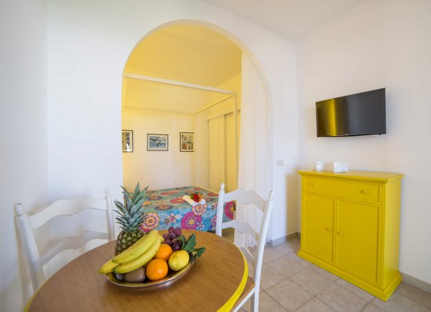 Tavolo rotondo con frutta, mobile giallo e letto colorato.