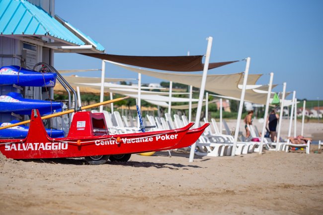 Una barca di salvataggio rossa sulla spiaggia con sedie a sdraio e ombrelloni.