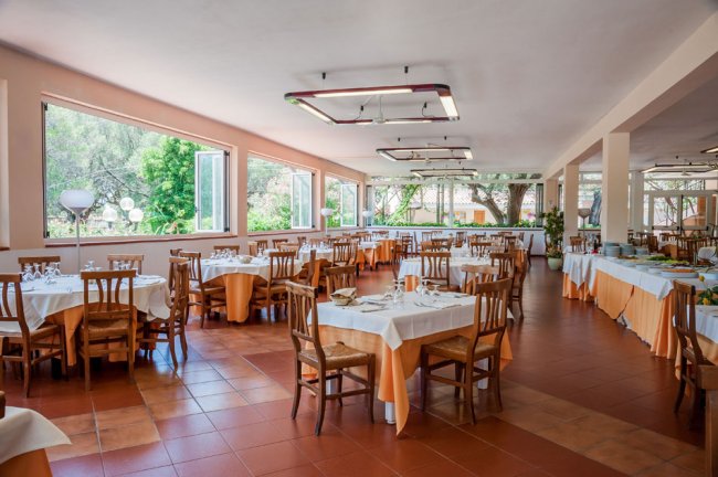 Interno di ristorante con tavoli apparecchiati di arancione e bianco, e grandi finestre luminose.