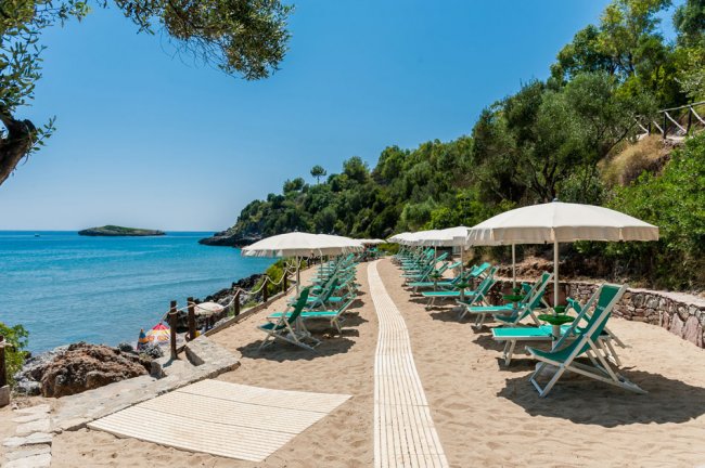 Spiaggia sabbiosa con lettini e ombrelloni bianchi vista mare e colline.
