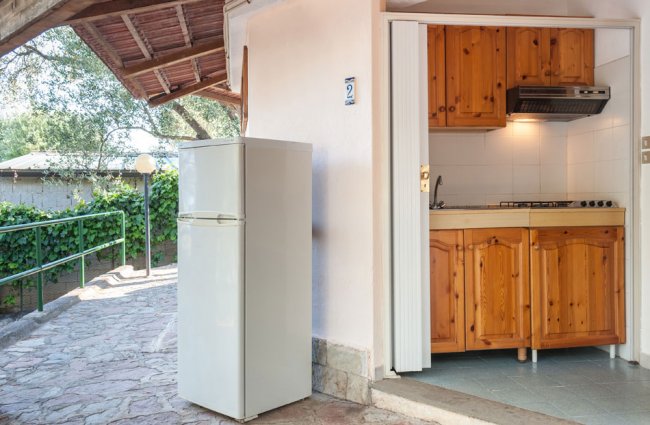 Una cucina all'aperto con pensilina, frigorifero bianco e mobili in legno.
