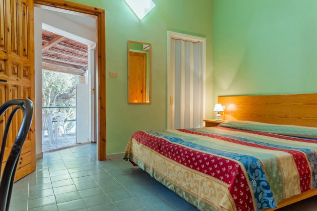 Camera da letto con pareti verdi, letto matrimoniale colorato e vista sul patio.