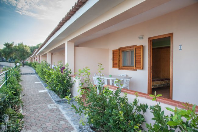 Struttura con portico lungo, giardino fiorito e pareti color pesca, tavolo e sedie all'esterno.
