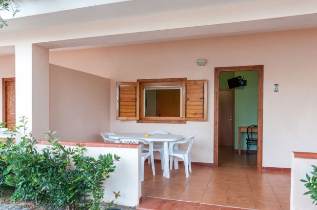 Una veranda con tavolo e sedie bianche, finestre e porta aperte su una stanza interna.