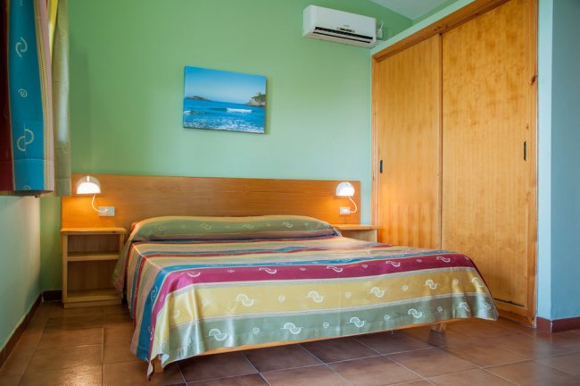 Camera con letto matrimoniale, copriletto a righe colorate e armadio a muro.