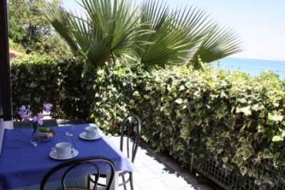 Tavolo apparecchiato con vista su una siepe verde e il mare.