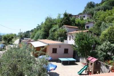 Vista di una casa rosa con tettoie e un piccolo parco giochi immerso nel verde.