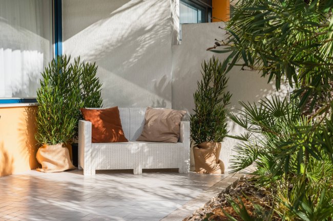 Angolo relax con divanetto bianco e piante in vaso su una terrazza.
