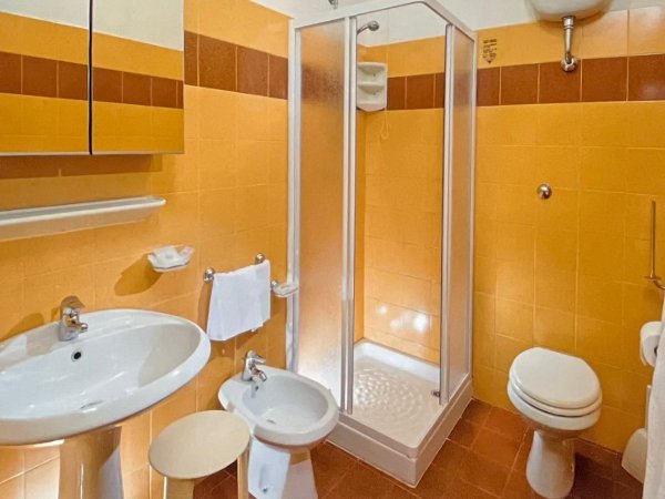 Bagno con piastrelle arancioni, doccia, lavabo, bidet e WC.