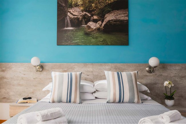 Letto matrimoniale con cuscini a righe, parete blu, foto di cascata e applique tonde.
