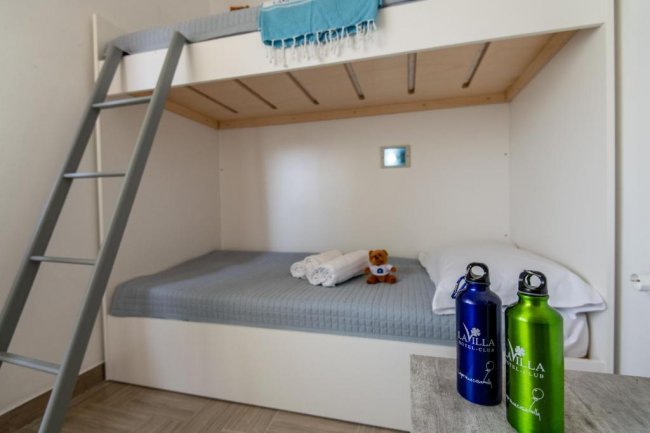 Letto a castello con lenzuola grigie, orsetto di peluche e due bottiglie riutilizzabili su tavolo.