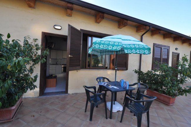 Un patio esterno con tavolo, sedie, ombrellone e piante in vaso.