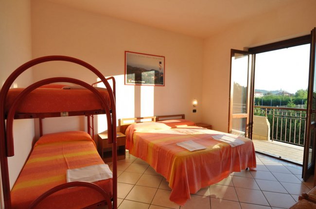 Camera con letto matrimoniale e letto a castello, porta finestra aperta su balcone.