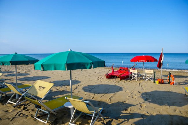 Spiaggia con ombrelloni verdi, sedie a sdraio gialle e canoe rosse.