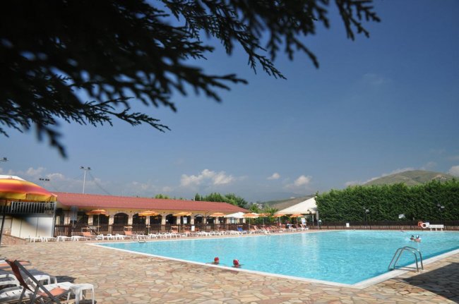 Ampia piscina all'aperto con lettini e tettoie circostanti.