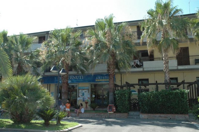 Edificio con palme e un'insegna blu. Persone sedute all'esterno. Cielo sereno.
