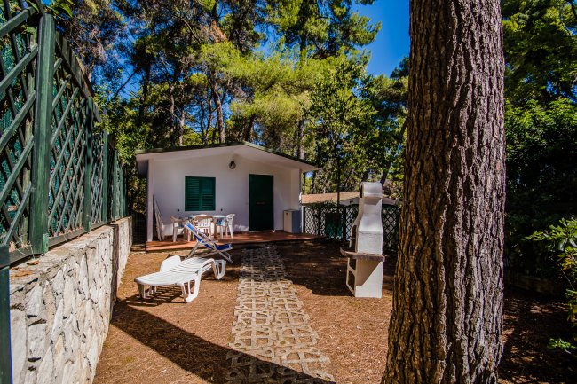 Veranda di una casa bianca nel bosco con lettini e barbecue.