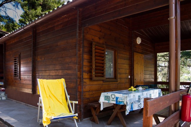 Una veranda in legno con lettino giallo e tavolo coperto da tovaglia con limoni.