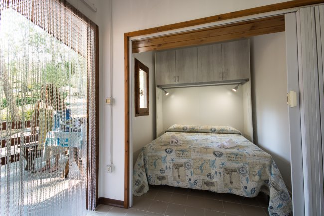 Stanza con letto matrimoniale, lenzuola a motivi blu, e porta a vetri con tenda a fili.