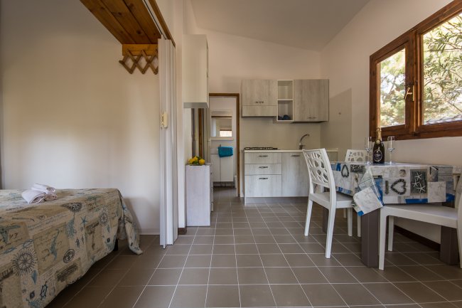 Interno di una cucina con tavolo, sedie e una finestra luminosa.