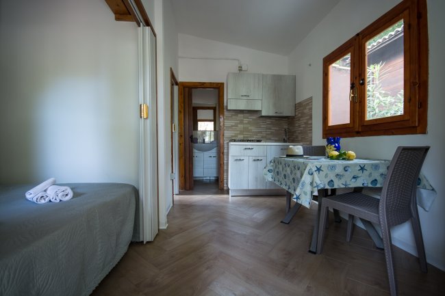 Cucina con tavolo, letto sulla sinistra e porta che conduce a un bagno.