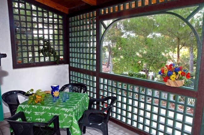 Terrazza coperta arredata con tavolo e sedie, decorata con fiori colorati in un portavasi.