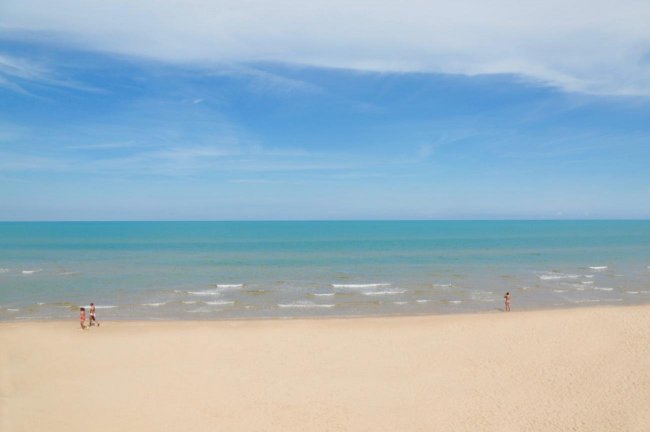 Spiaggia di sabbia fine con mare calmo e cielo azzurro.