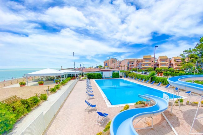 Piscina con scivolo accanto al mare e palazzi.