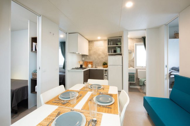 Sala da pranzo e cucina in un interno moderno, con tavolo apparecchiato e divano blu.