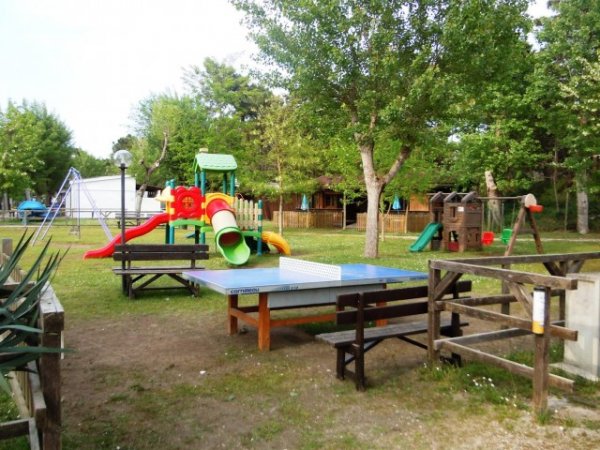 Area giochi con scivoli e tavolo da ping pong, circondata da alberi e staccionate di legno.