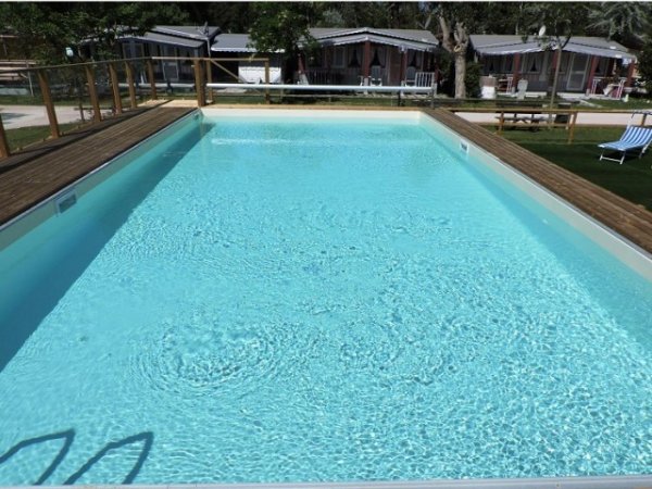 Una piscina all'aperto con acqua limpida, circondata da un'area con sdraio e alberi.