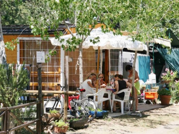Persone sedute sotto un ombrellone bianco fuori da una casetta di legno.