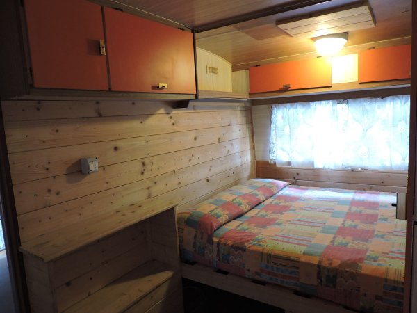 Camera da letto con pareti in legno, letto matrimoniale e mobili arancioni.