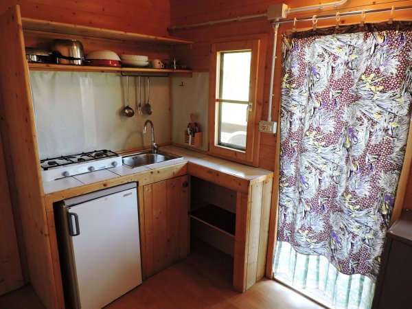 Cucina compatta in legno con lavello, fornello, mini frigo e mensole.