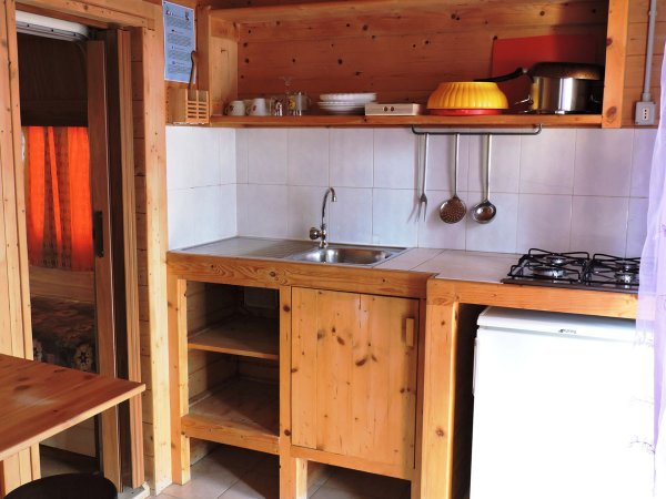 Piccola cucina in legno con lavello, piano cottura, e frigorifero.