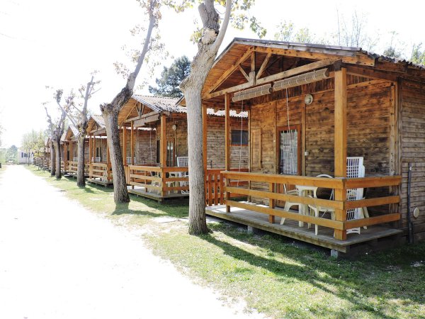 Serie di bungalow di legno con portici e sedie bianche su un prato.