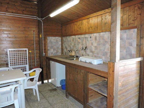 Cucina in legno con lavello, frigorifero e fornello. Tavolo con sedie bianche.