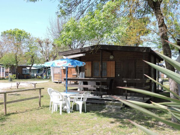 Bungalow in legno con terrazza, tavolo, sedie e ombrellone nel giardino.