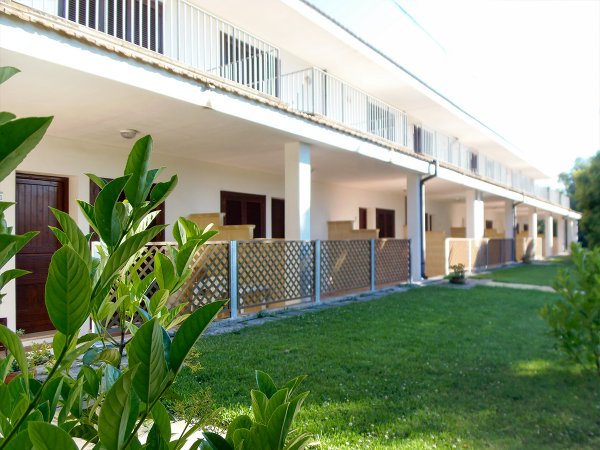 Un edificio bianco con balconi e un giardino verde in primo piano.