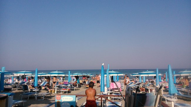 Spiaggia affollata con ombrelloni blu e persone che prendono il sole.