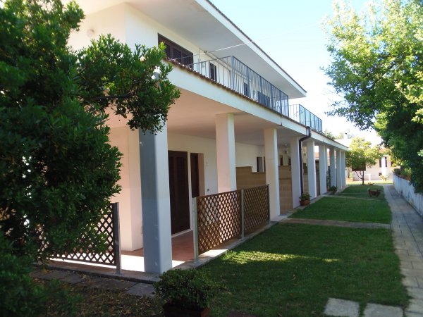Una casa a due piani con portico, giardino e balcone lungo il primo piano.