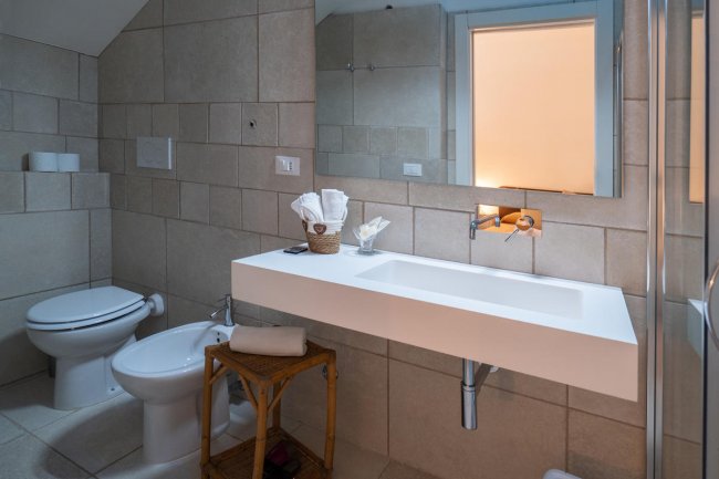Bagno moderno con lavabo bianco, bidet e WC, pareti piastrellate color beige.