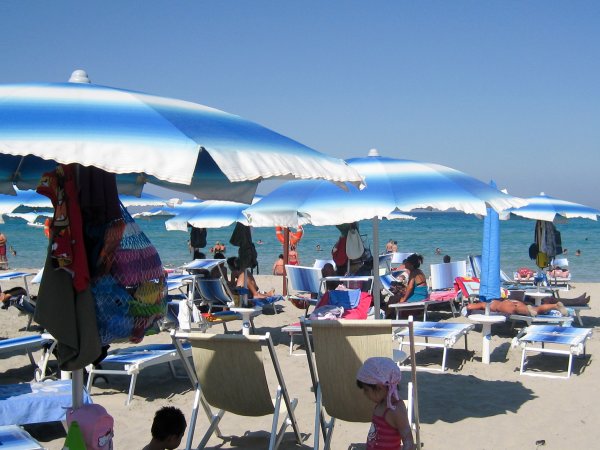 Ombrelloni blu su una spiaggia affollata con persone che prendono il sole.