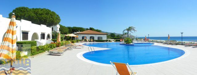 Piscina circondata da sdraio e ombrelloni, vista mare e cielo azzurro.