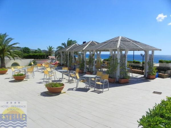 Area esterna con gazebo e sedie gialle, circondata da piante e vista mare.