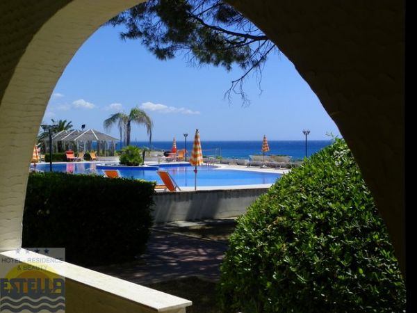 Piscina con vista mare, ombrelloni e piante.