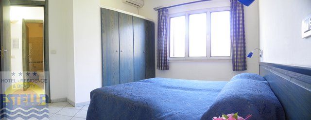 Camera con letto matrimoniale blu, finestra, armadio e tende a quadri.