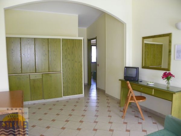 Una stanza d'albergo con armadio verde, scrivania con specchio, sedia e TV.