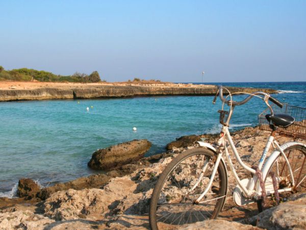 Bicicletta bianca parcheggiata su rocce vicino a una baia con acqua turchese.